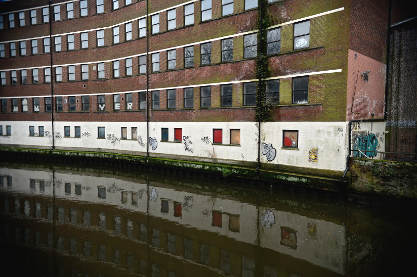 Photo of an old apartment building with graffiti by the Wenzum river in Norwich, England