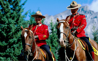 Photo of two men on horses with red uniforms and wide brimmed hats