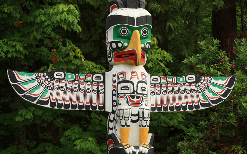 Photo of a totem pole with a bird carved into it and painted in bright colours